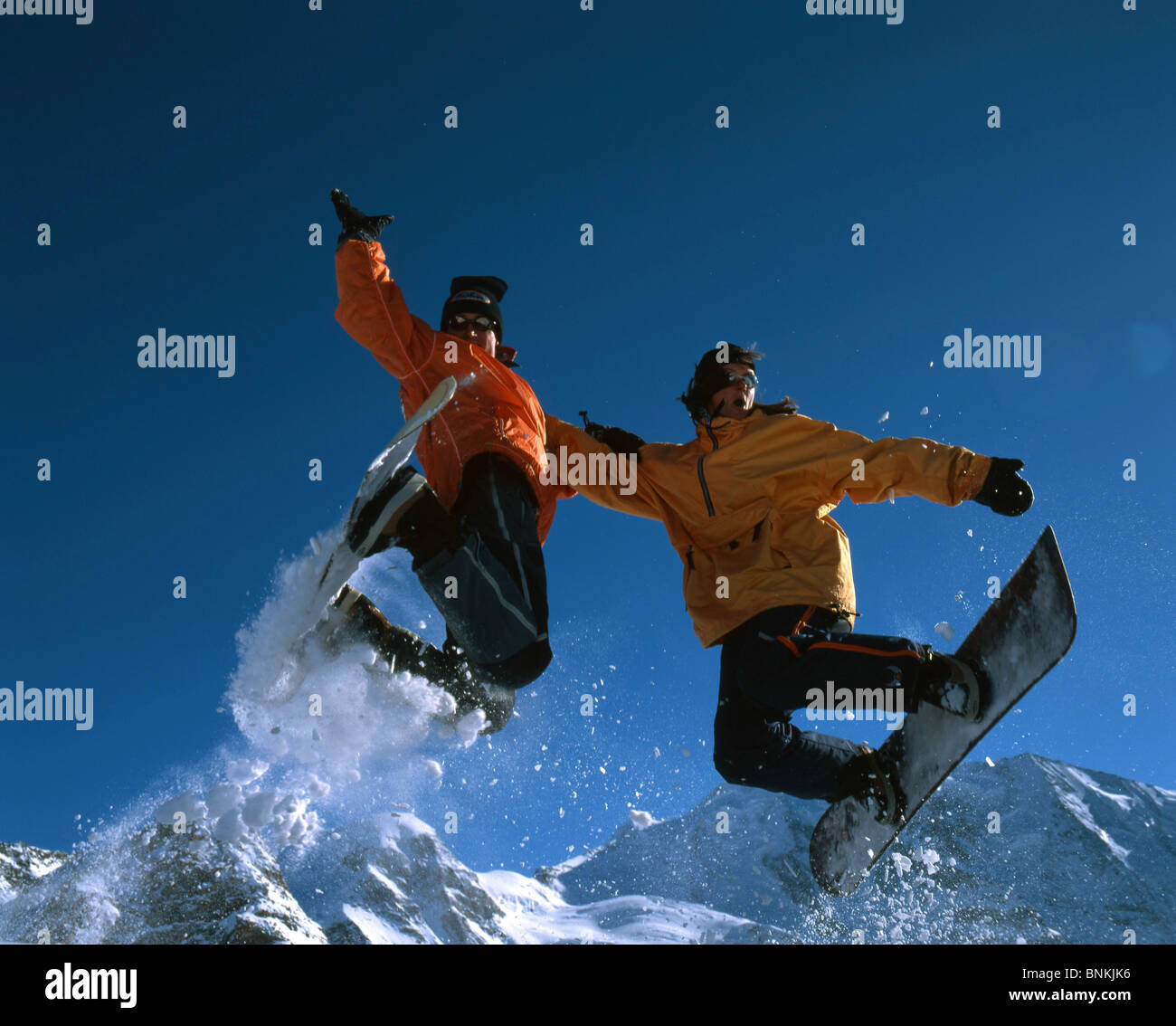 Switzerland winter sports persons two pair couple mountains jump Snow boarder snowboard orange freeride caper blue sky heaven Stock Photo