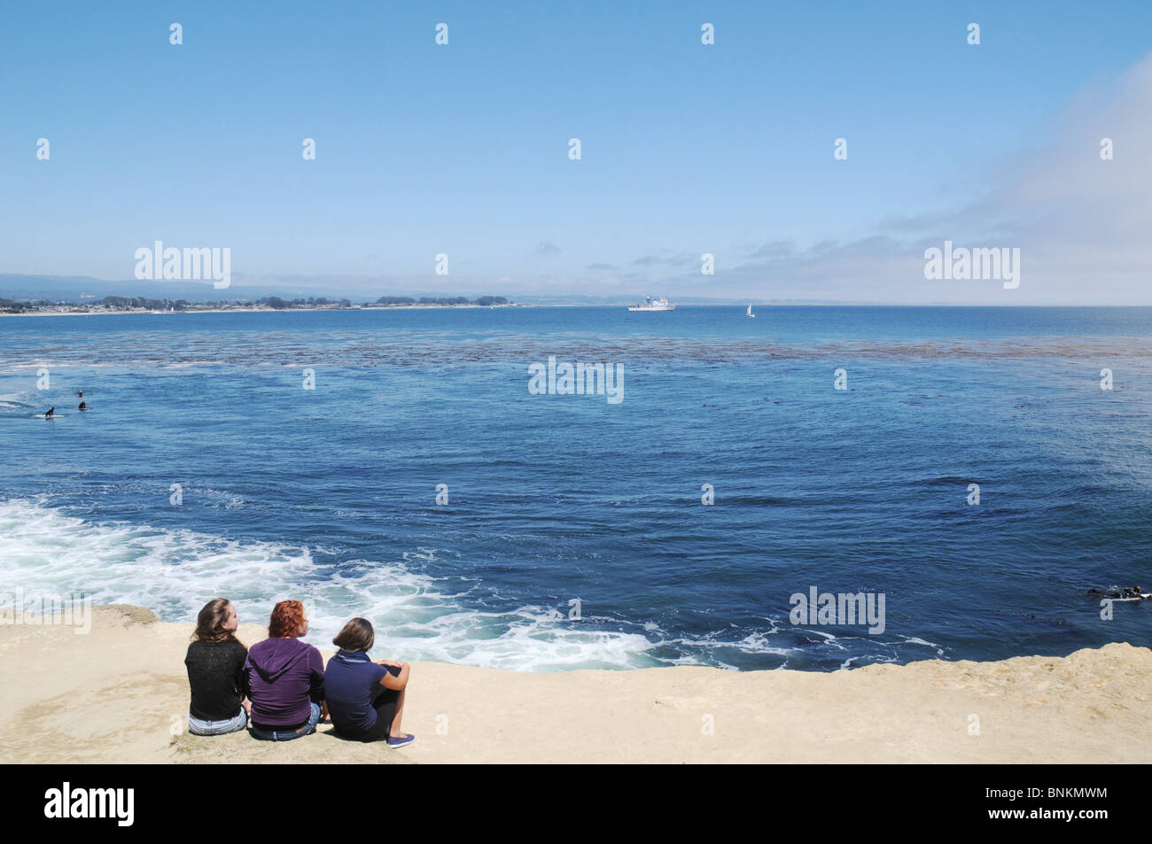 Three teenage girls watching the surf from a ledge on westcliff drive in santa cruz ca USA at Lighthouse field Stock Photo