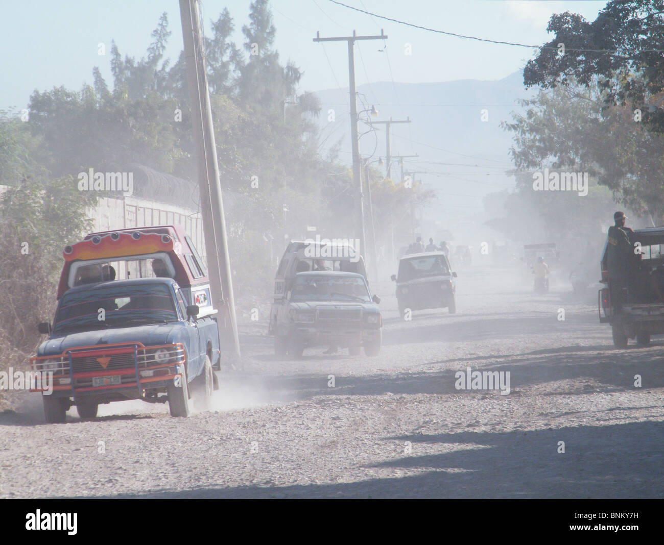 Cars drive through clouds of dust, left behind by hurricane-related flooding in 2008, in Gonaives, Haiti Stock Photo