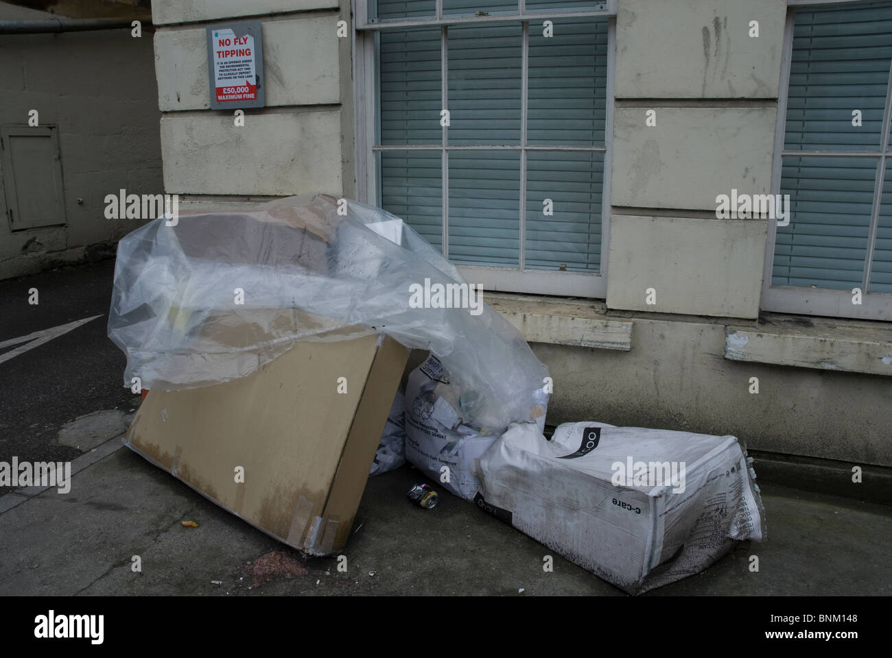 Fly tipping under a sign saying no fly tipping, on the London Road, Bath Somerset UK Stock Photo