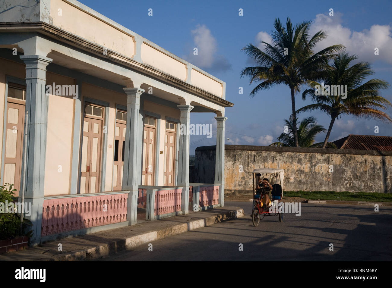 Cycle rickshaw passing a colonial house in Baracoa, Cuba Stock Photo