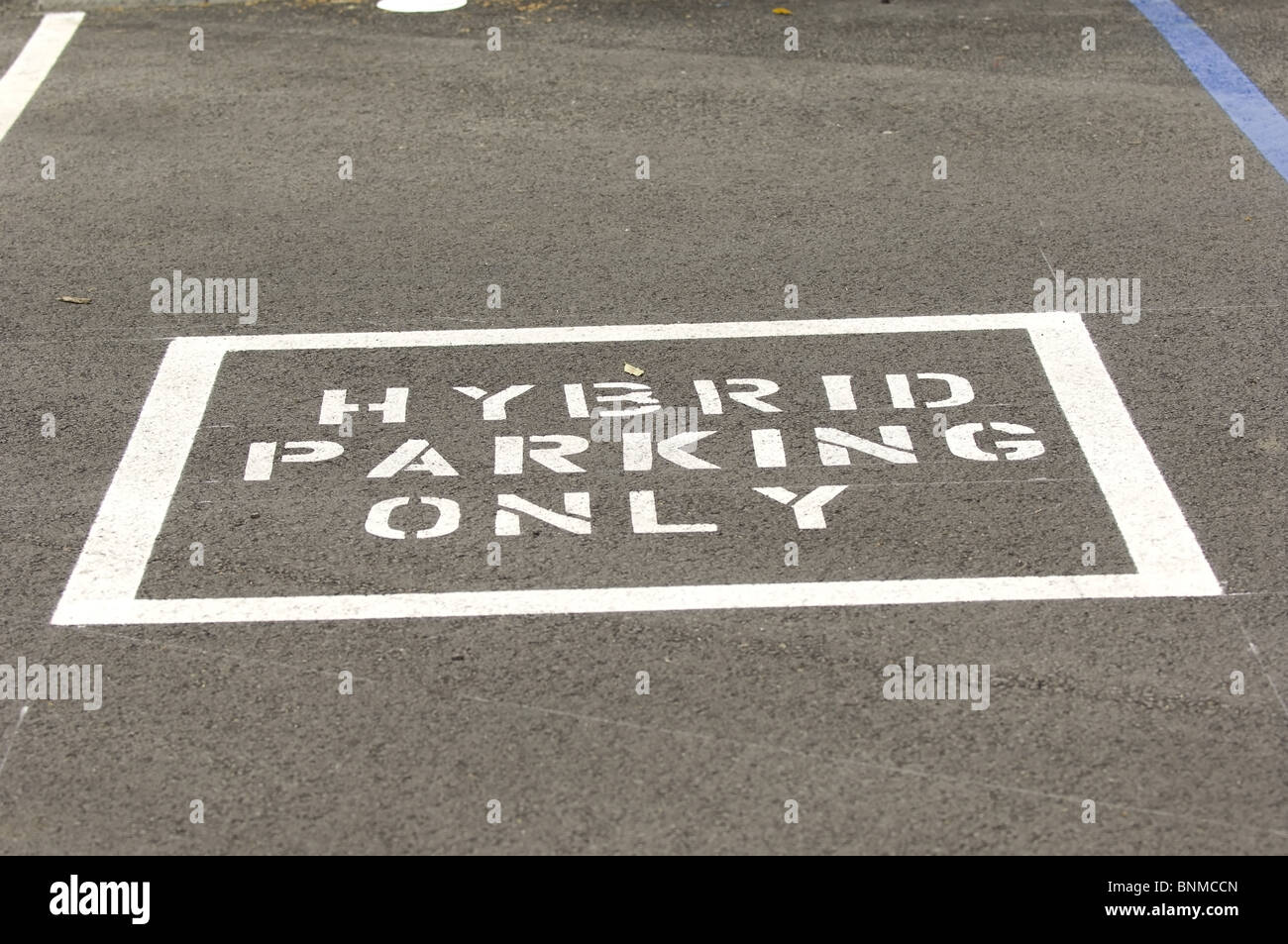 'Hybrid Parking Only' sign is painted in a parking lot designating parking that is reserved for hybrid vehicles only. Stock Photo