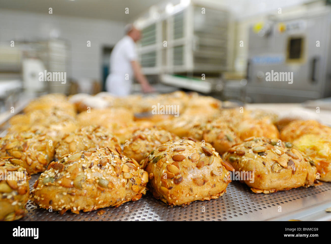 completed bread rolls in front, blurred working baker behind Stock Photo