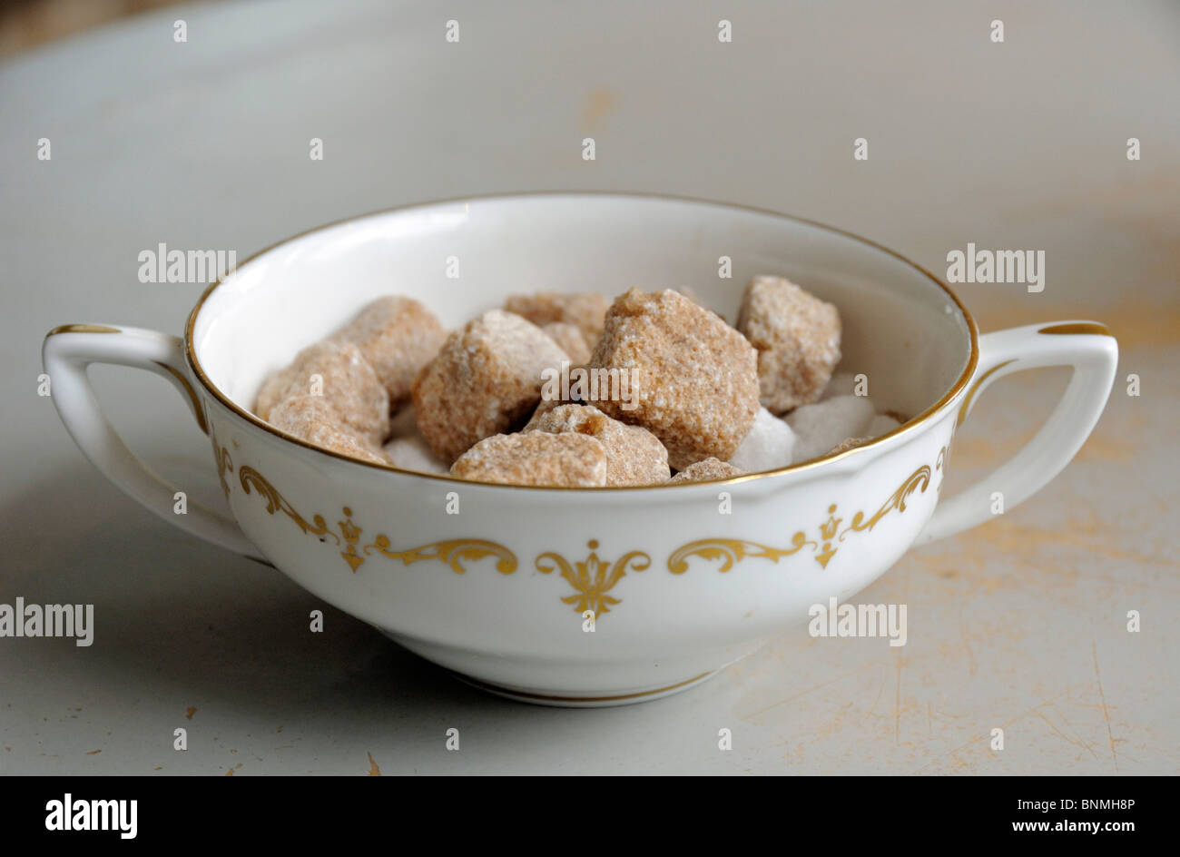 Chunky cubes of brown sugar in a vintage white and gold two handled bowl Stock Photo