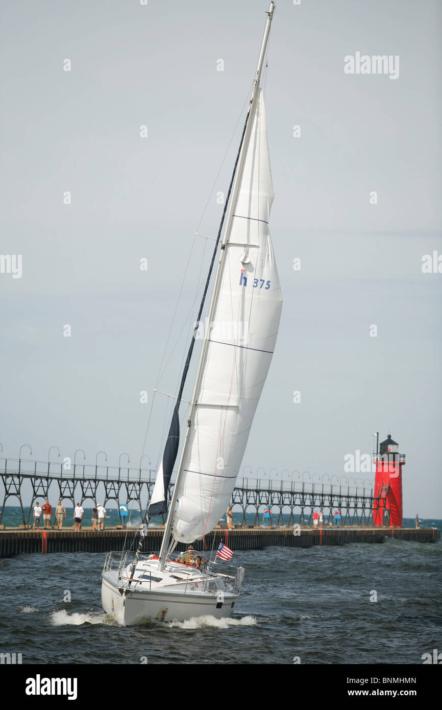 sail boat sails along the pier and lighthouse from Lake Michigan into the Black river in South Haven Michigan Stock Photo