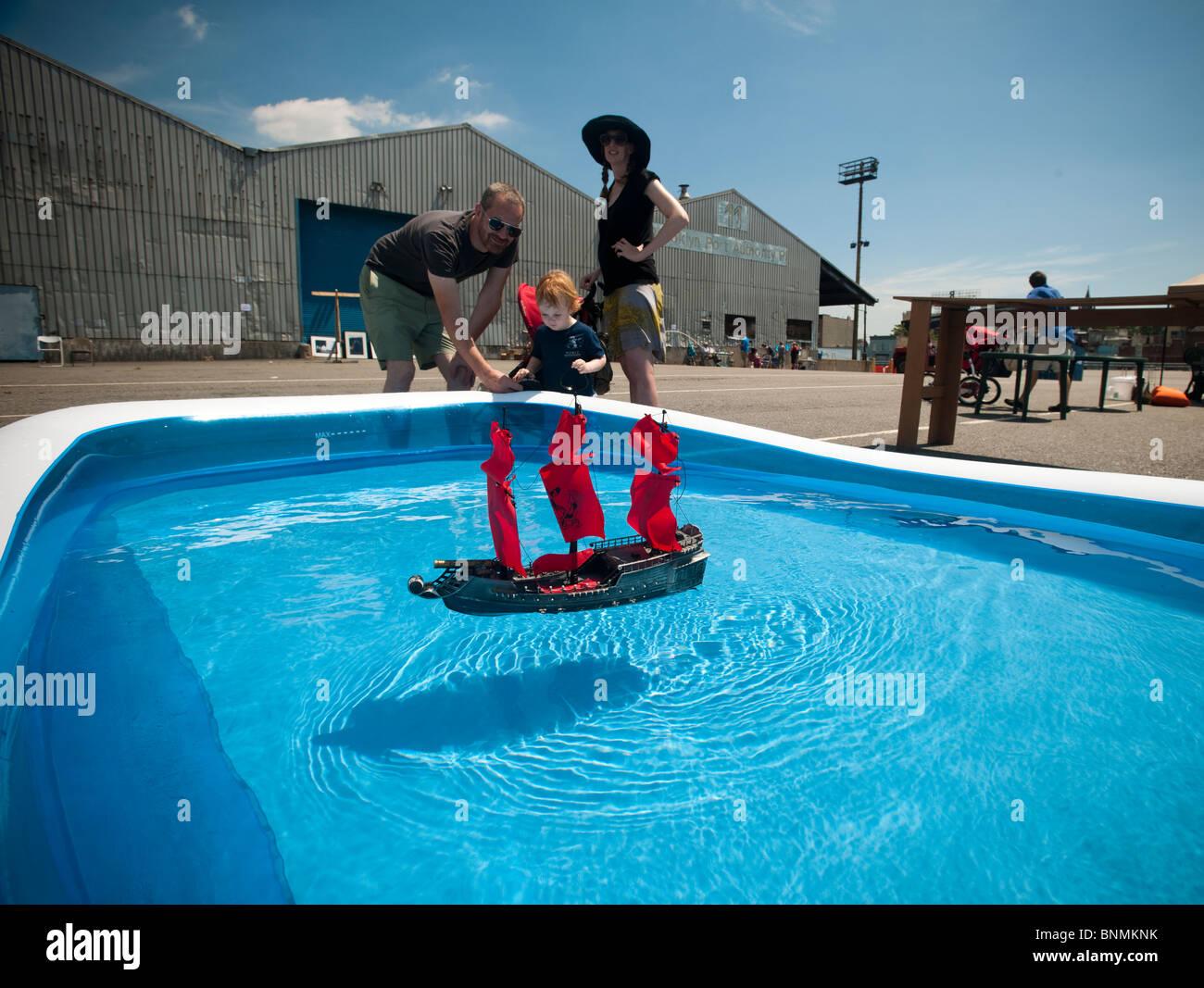 A family uses a radio control to maneuver a radio controlled toy boat
