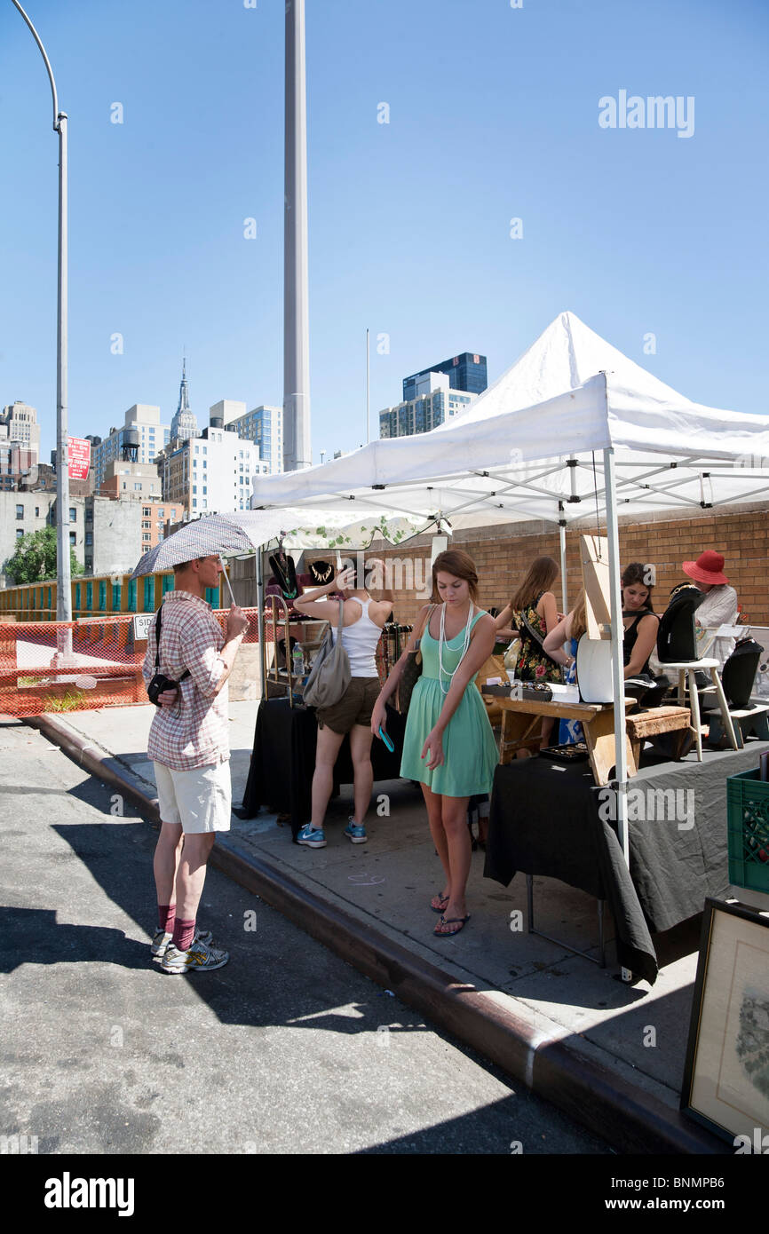 man waits patiently shaded by umbrella as his pretty girlfriend considers buying rope of pearls at Hells Kitchen flea market Stock Photo