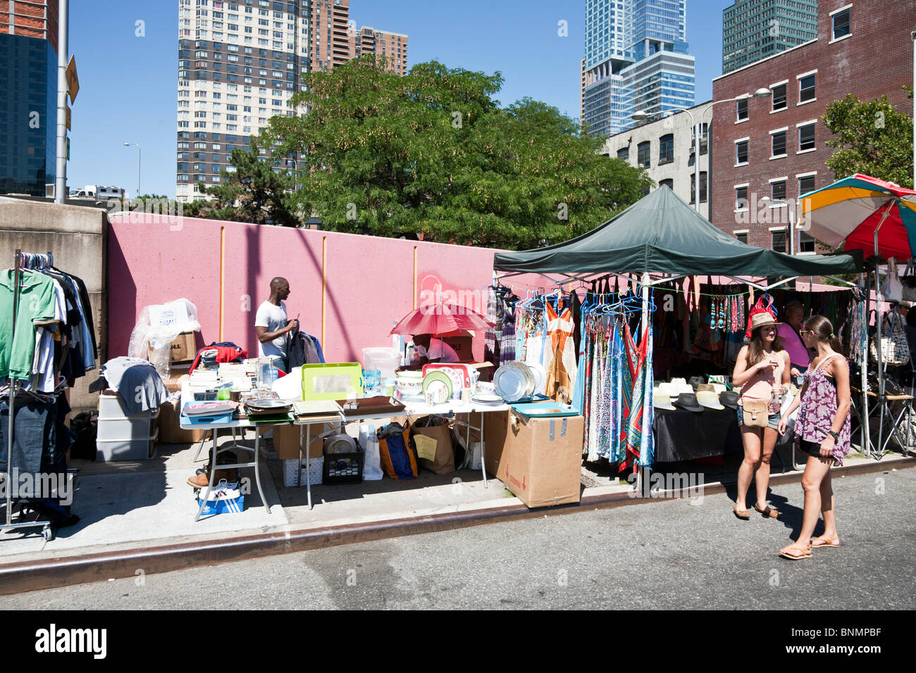 two pretty girls chatting in front of stalls selling recycled  & specialty clothing & other items at Hells Kitchen flea market Stock Photo