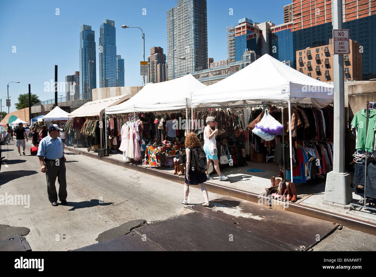 people stroll west 39th street browsing stalls selling recycled clothing  & furs at Hells Kitchen weekend flea market New York Stock Photo