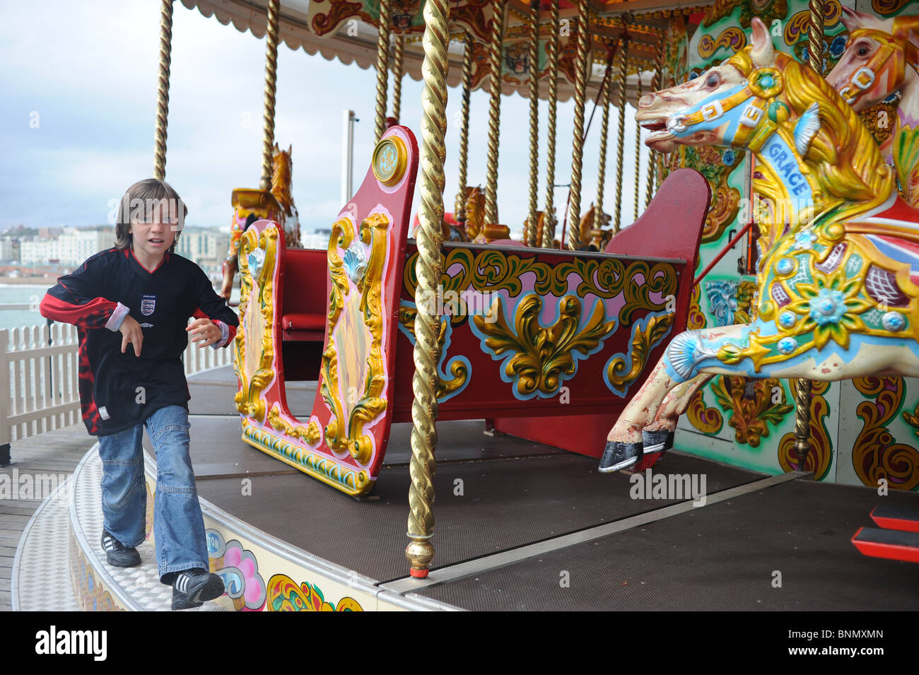 Boy 10-11 running round merry-go-round on Brighton Pier Stock Photo