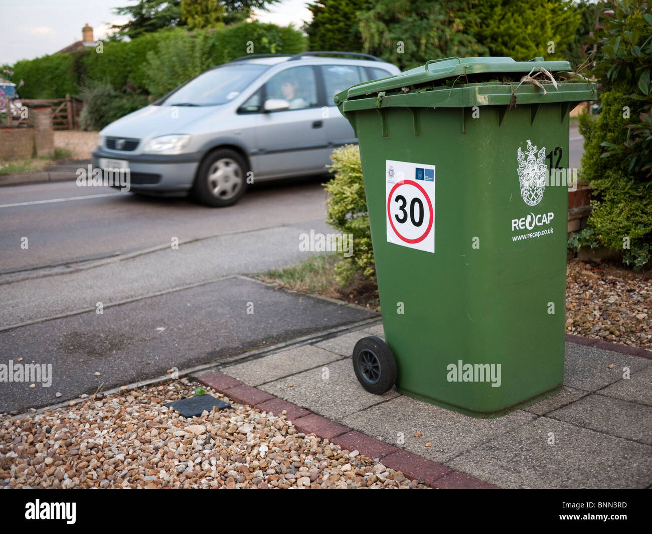 30 mph Speed limits signs on wheellie bins in South Cambridgeshire village, showing road with moving car going by Stock Photo