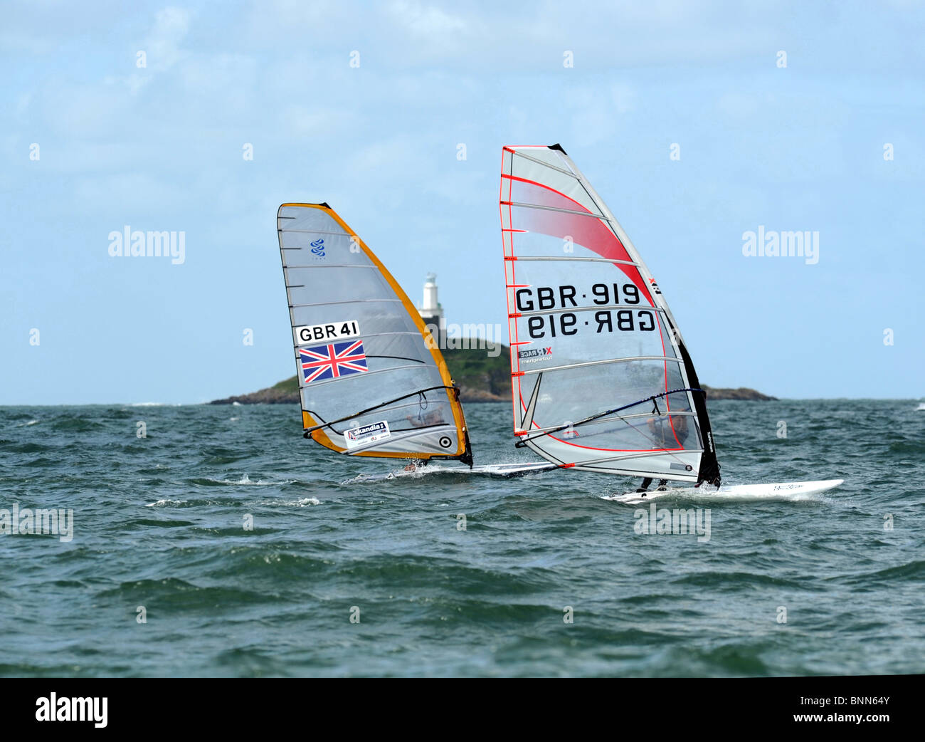 Two windsurfers race across the bay with Mumbles lighthouse in the background Stock Photo