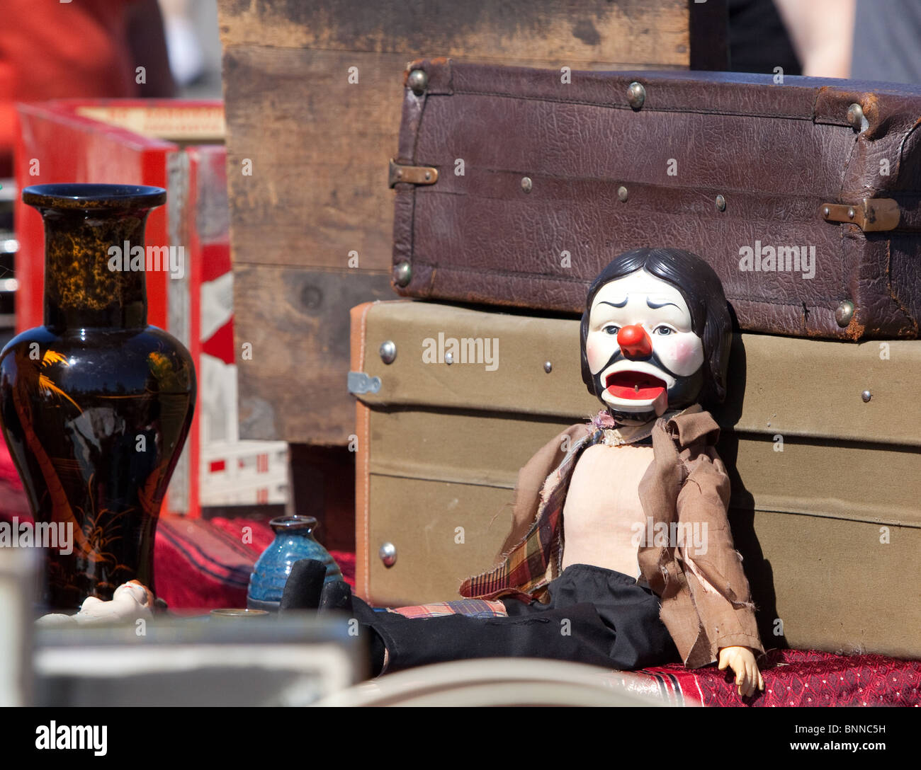 Creepy antique doll leaning on an old trunk at a flea market. Stock Photo