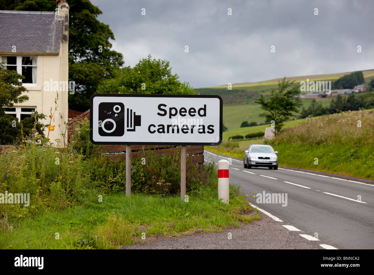 A UK speed camera sign at the side of an A road with a silver car going past. Stock Photo