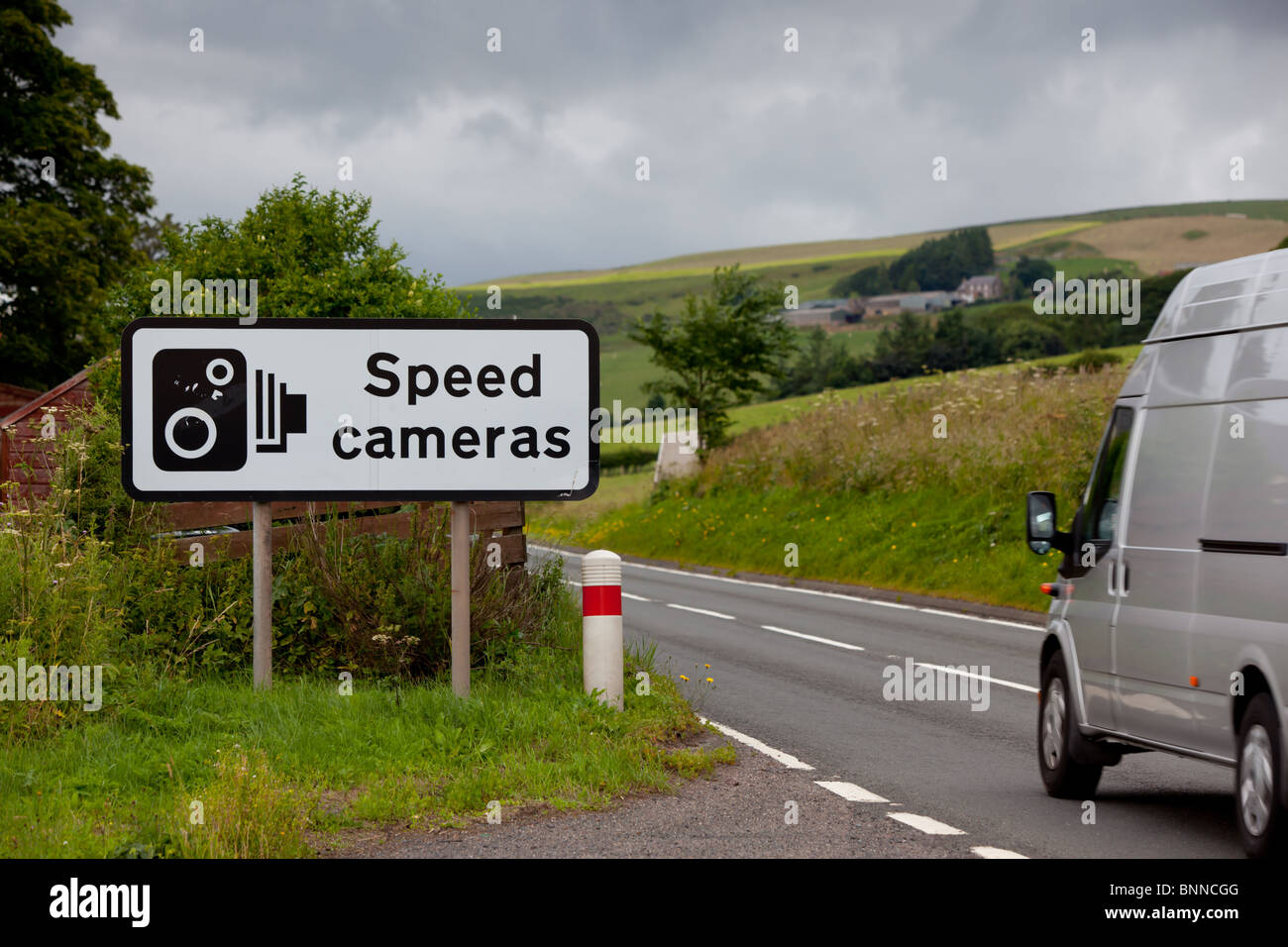 A UK speed camera sign at the side of an A road with a silver van going by Stock Photo