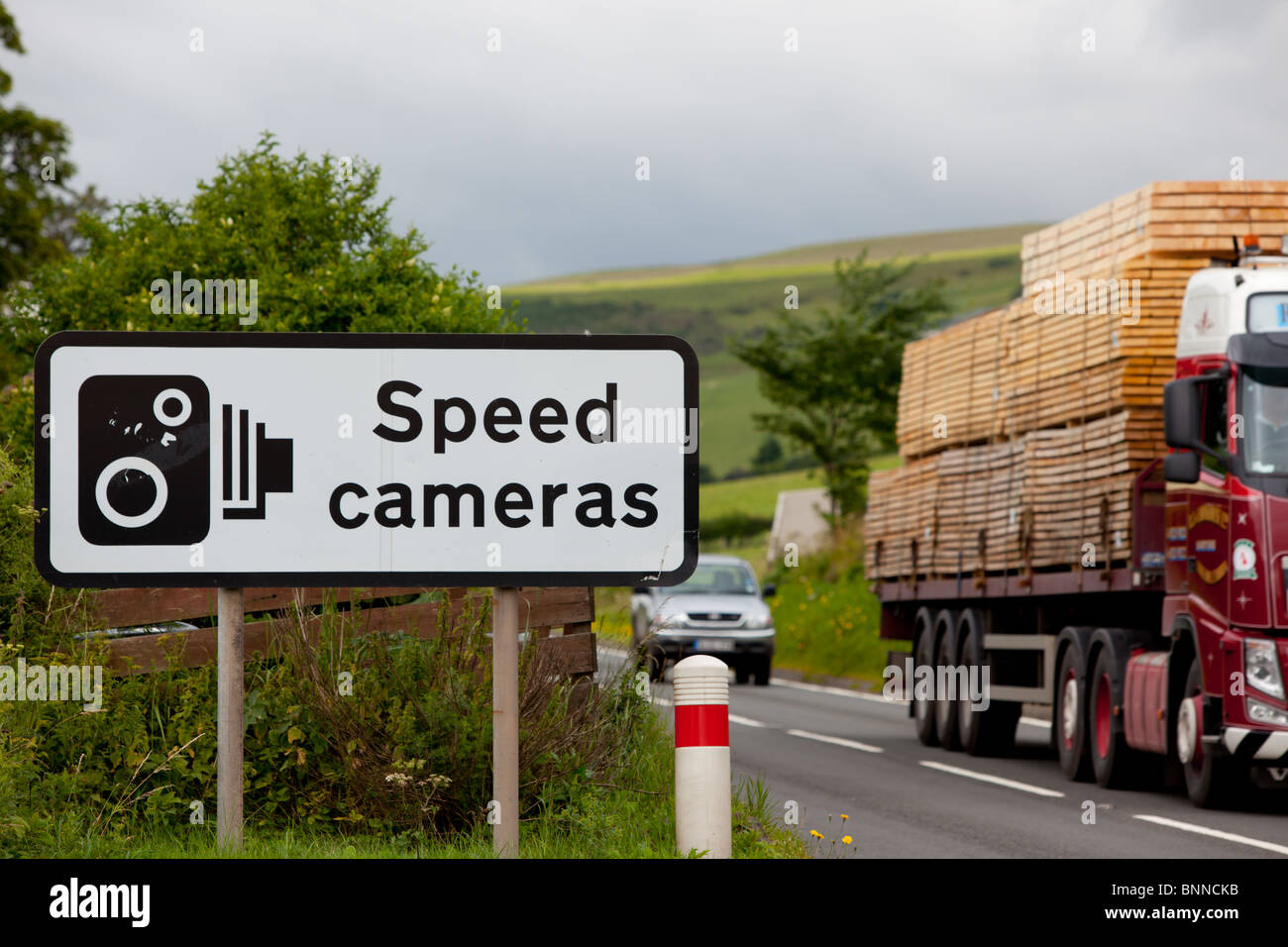 A UK speed camera sign at the side of an A road with a lorry going past. Stock Photo