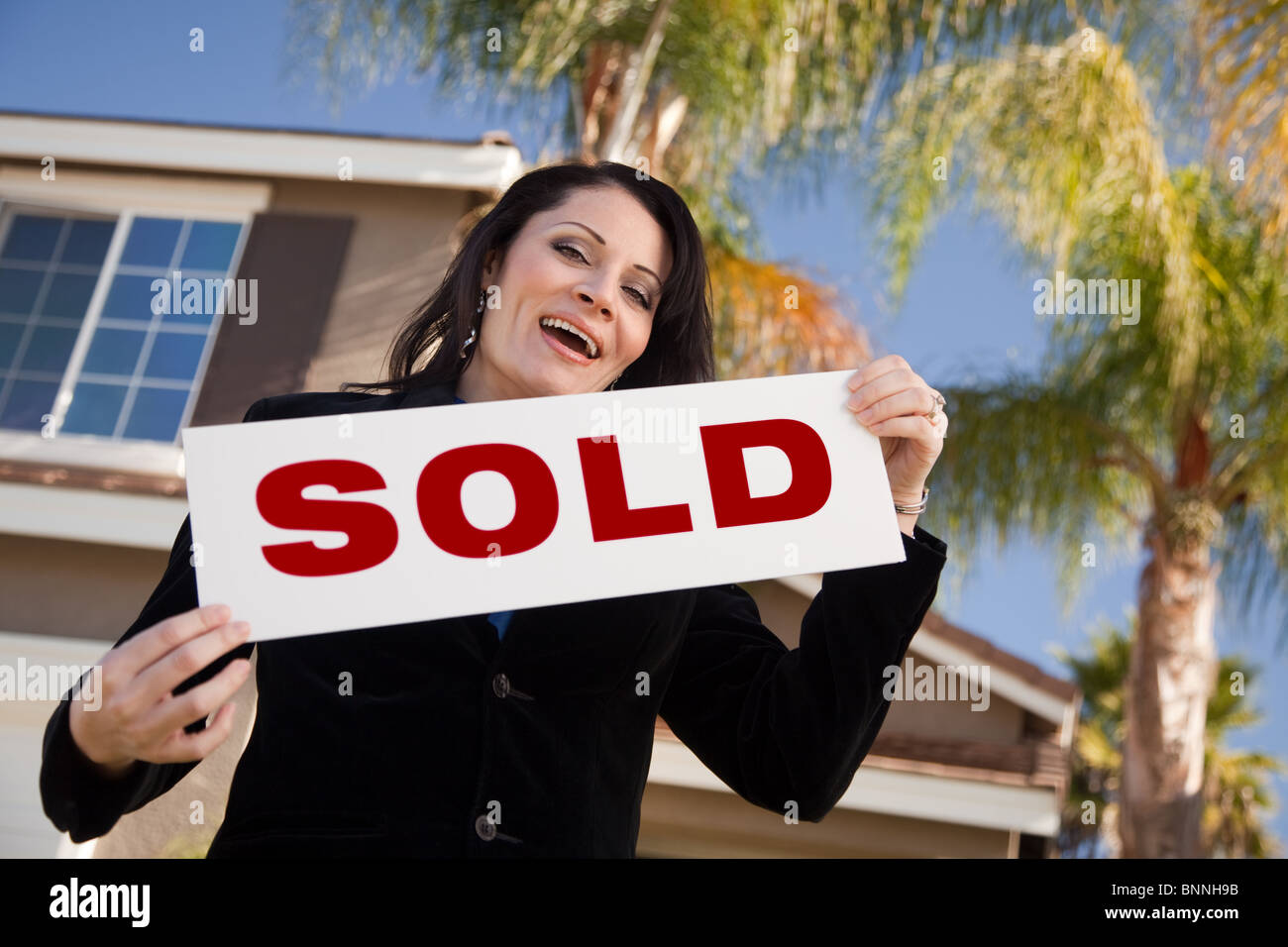 Happy Attractive Hispanic Woman Holding Sold Sign In Front of House ...