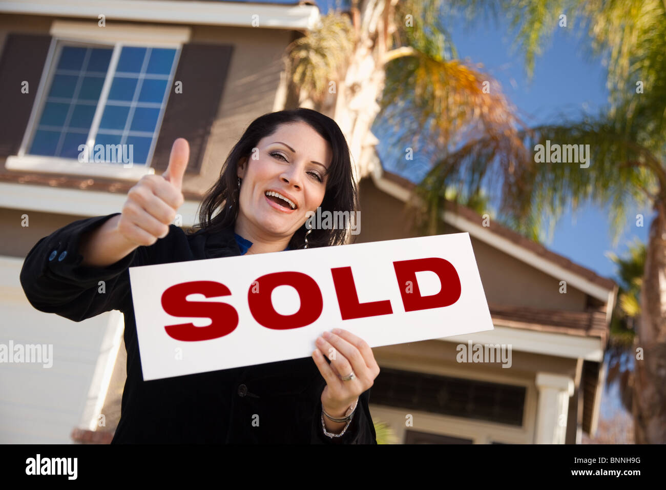 Happy Attractive Hispanic Woman with Thumbs Up Holding Sold Sign In ...
