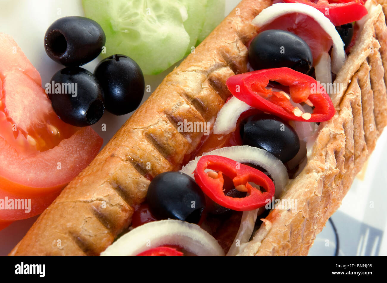 Closeup of hot dog with vegetables. Fast food, tomato, hot pepper, onion, sausage, grilled roll
