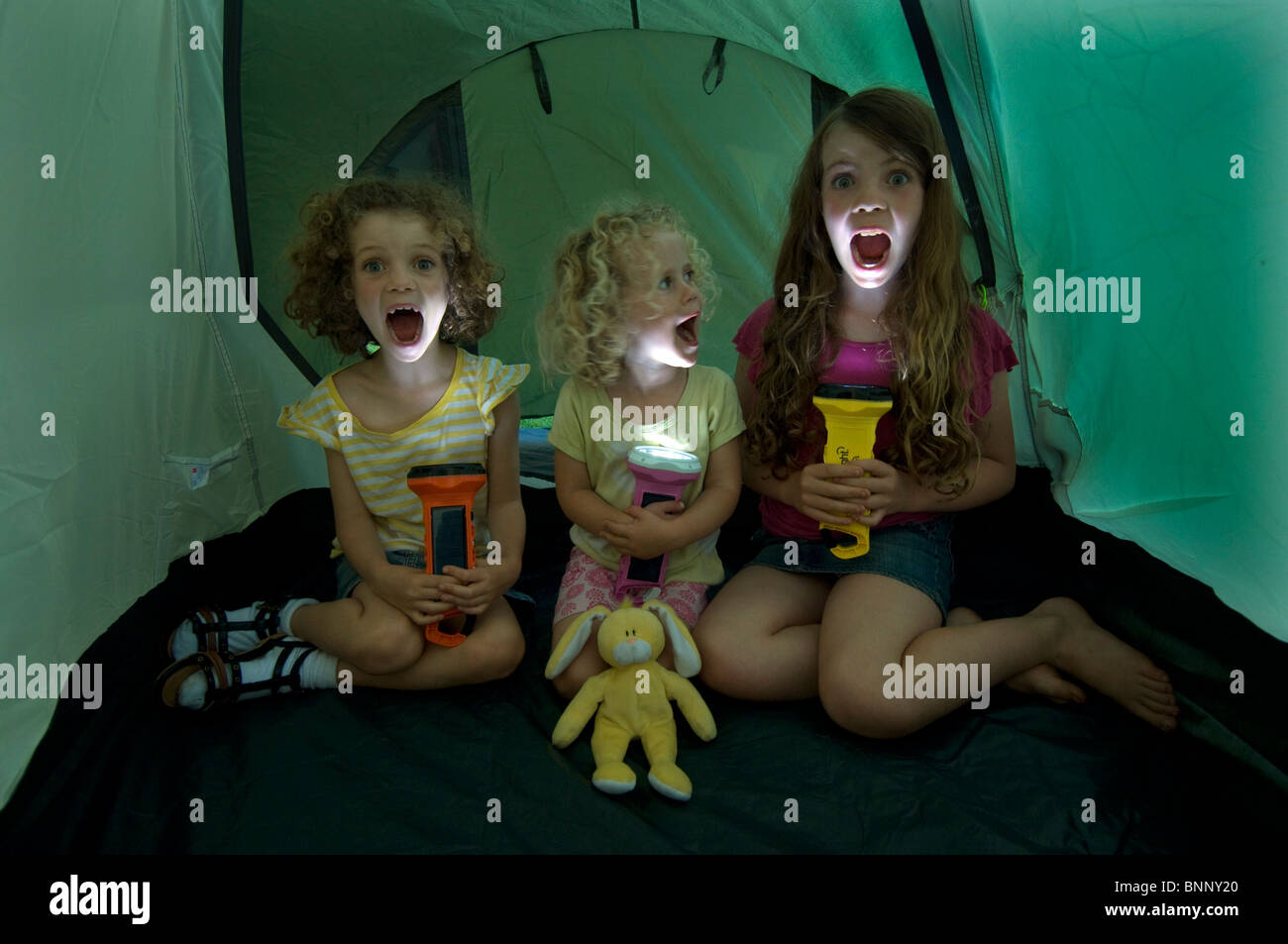 Three little girls in a tent giving themselves spooky faces with solar powered Alamy torches. Stock Photo