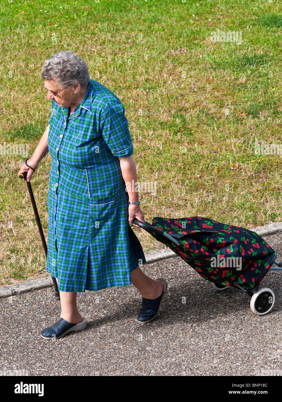 Elderly woman with shopping trolley walking along pavement - France. Stock Photo
