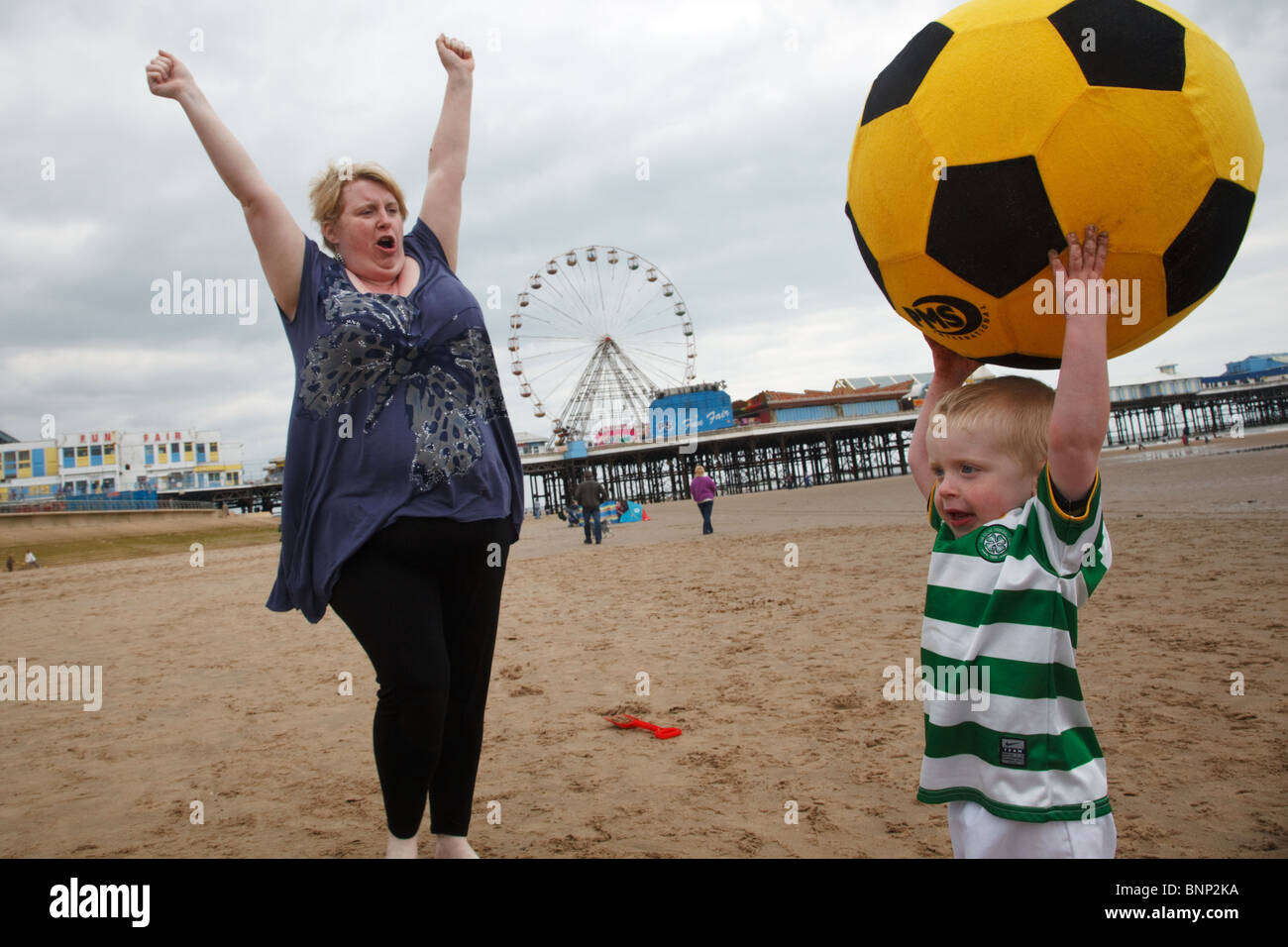 A little boy dressed in a football uniform with a large ball on the beach in Blackpool, England. Stock Photo