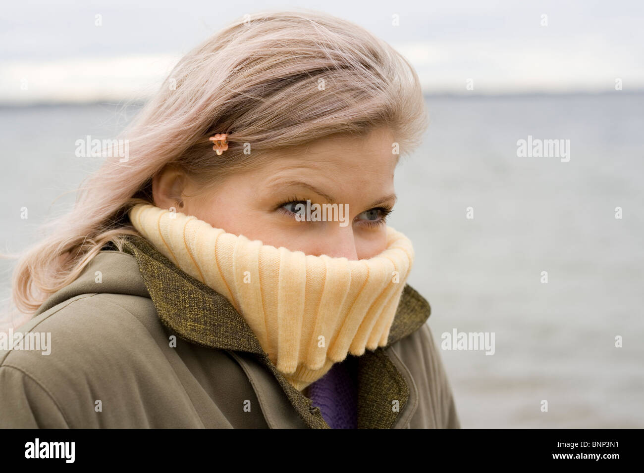 Really cold! A blond girl in a coat and sweater portrait on cold wind. Lake in a background. Stock Photo