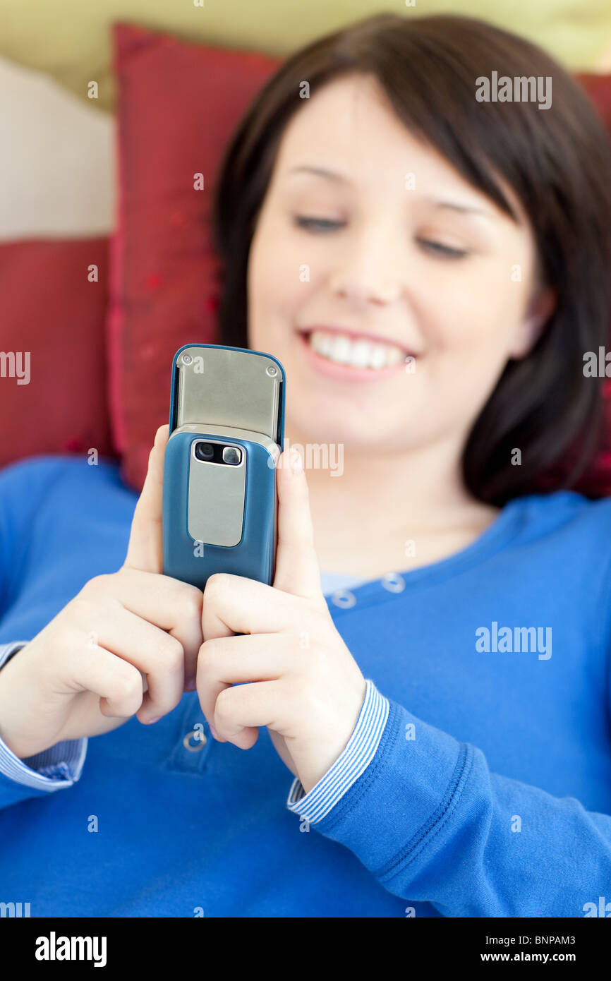Cheerful teen girl sending a text lying on a sofa Stock Photo
