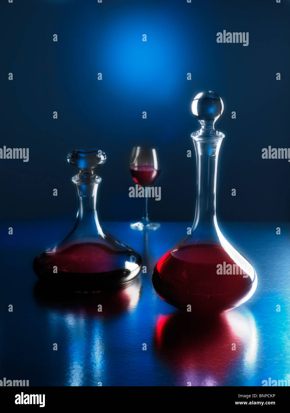 Two moonlit decanters with red wine and glass in background with reflections Stock Photo