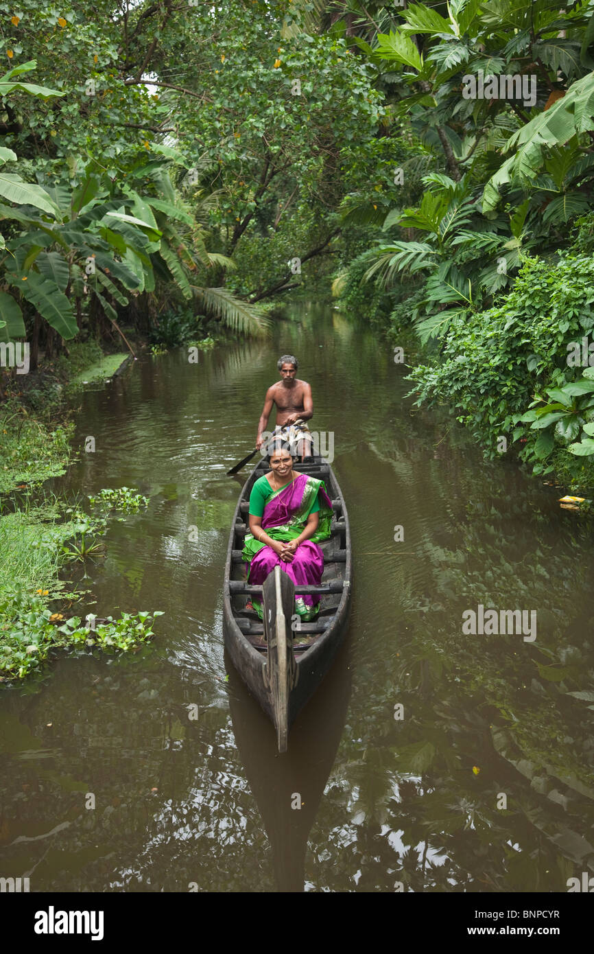 Man rowing India tourist woman with bright purple and green sari on a wooden canoe along the beautiful scenic backwater canals Stock Photo
