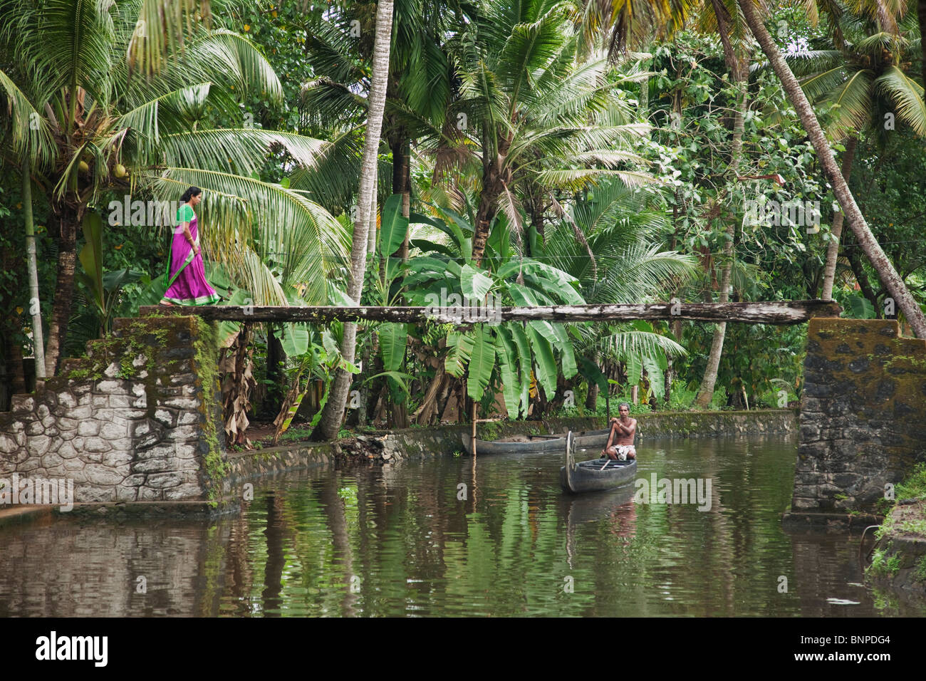 Woman with bright purple and green sari walking over a beautiful scenic canal bridge in Alappuzha, Kerala, India. Model released Stock Photo