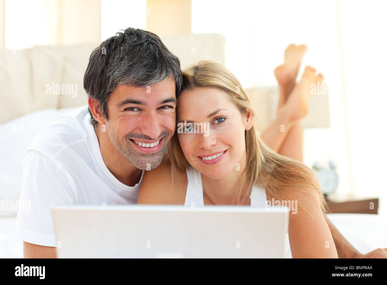 Enamoured couple using a laptop lying on bed Stock Photo - Alamy
