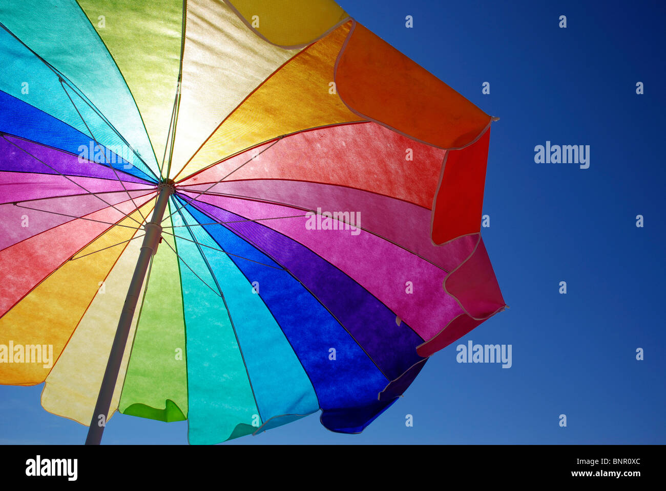Rainbow colored sun umbrella at the beach against clear blue sky. Stock Photo