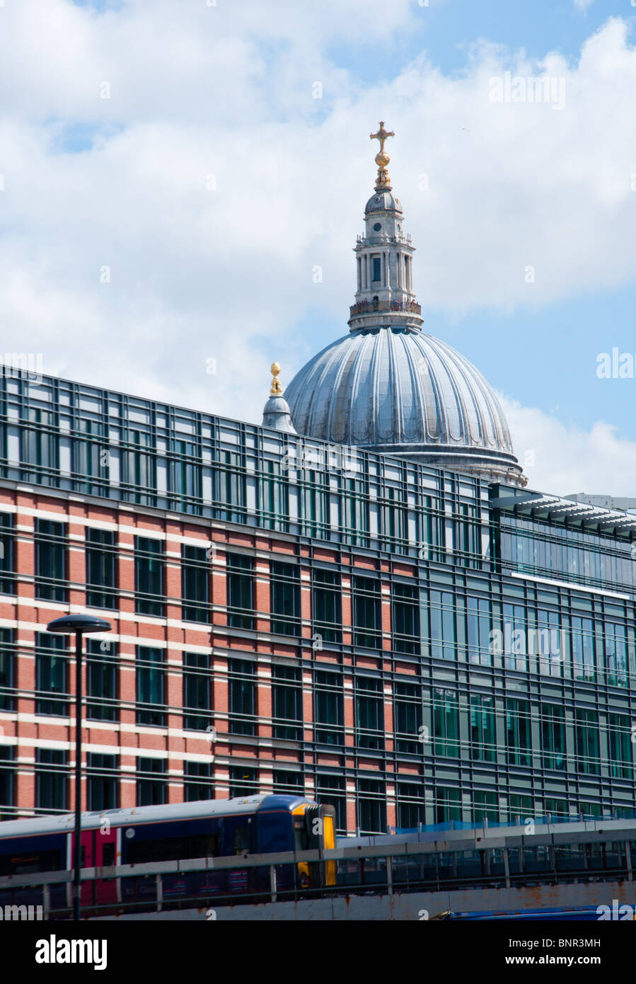 St Paul's Cathedral seen over modern buildings as a train goes past. Stock Photo