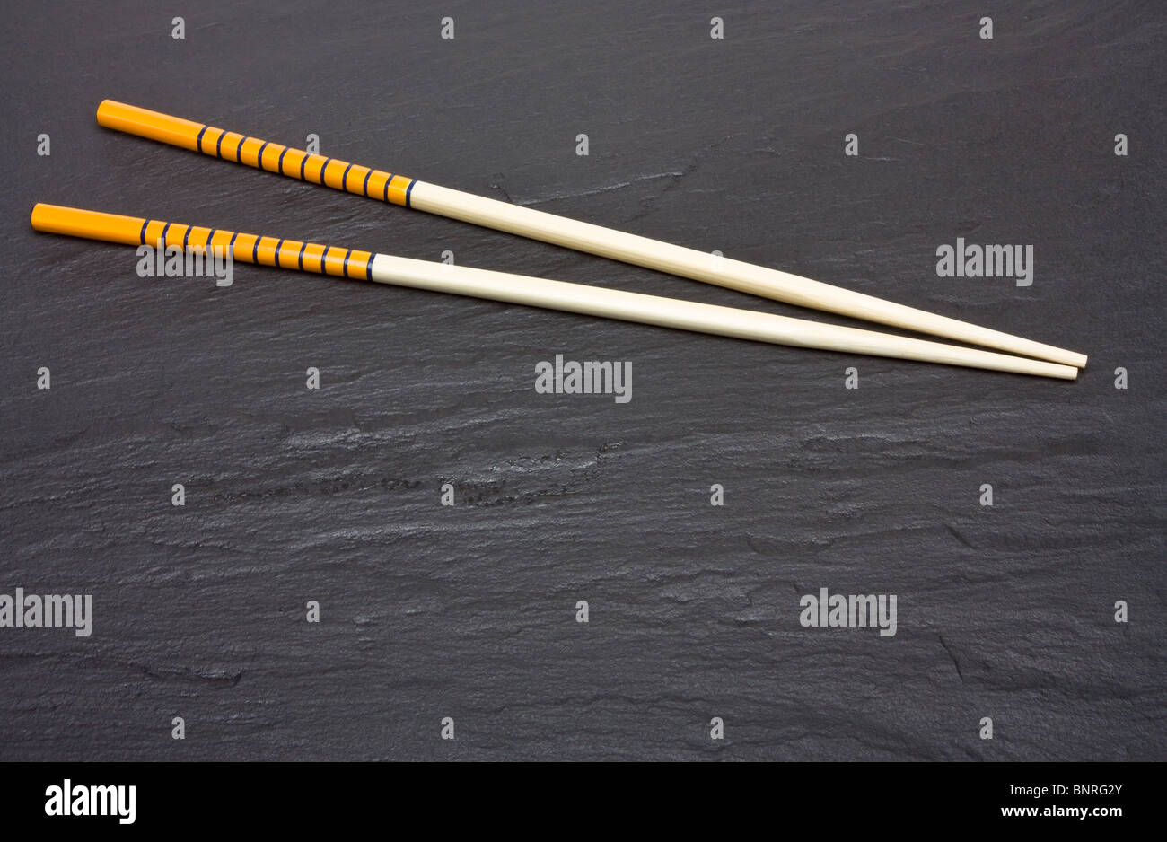 Pair of vibrant orange chopsticks from low perspective isolated on dark slate background. Stock Photo