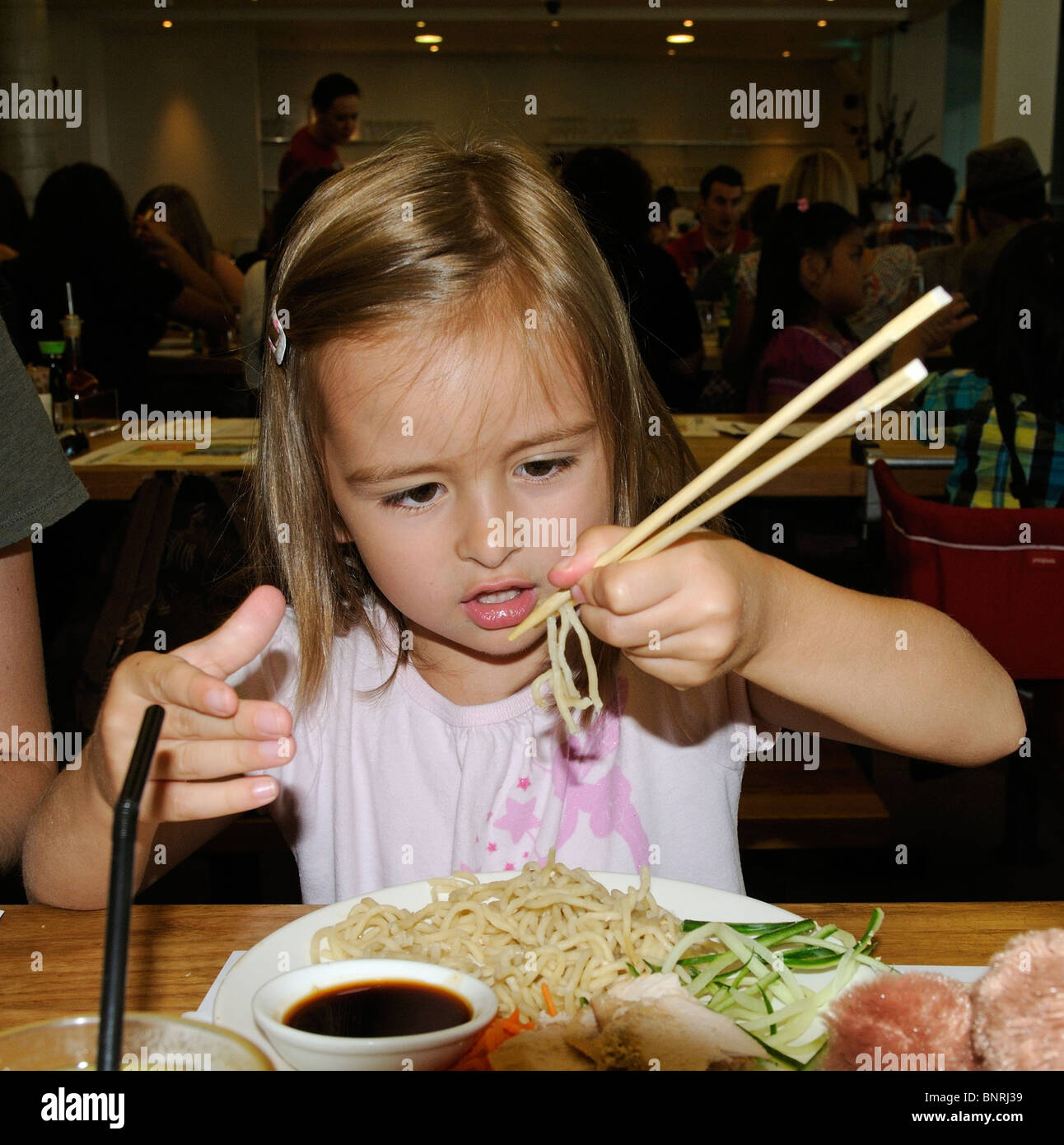 Little girl eating noodles in a restaurant and using chopsticks Stock Photo