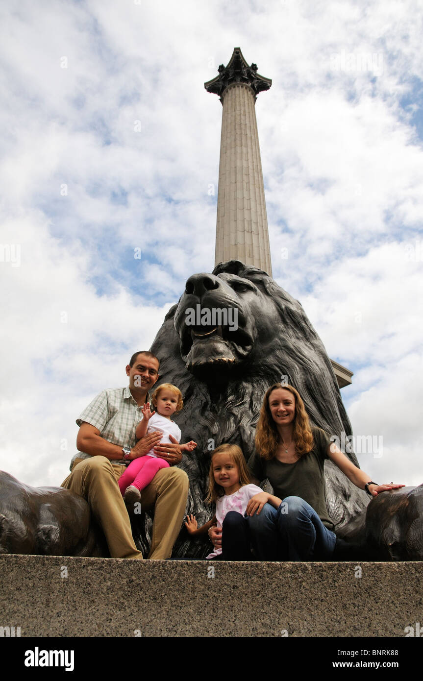 Family visiting London pose with a lion on Trafalgar Square below Nelson's Column Stock Photo