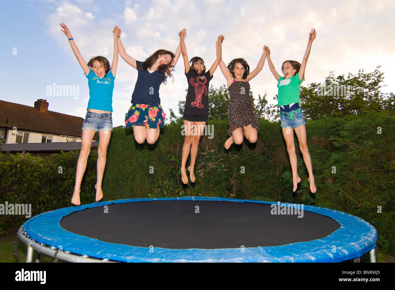 Horizontal close up portrait of a group of girl friends jumping on a  trampoline in a garden Stock Photo - Alamy