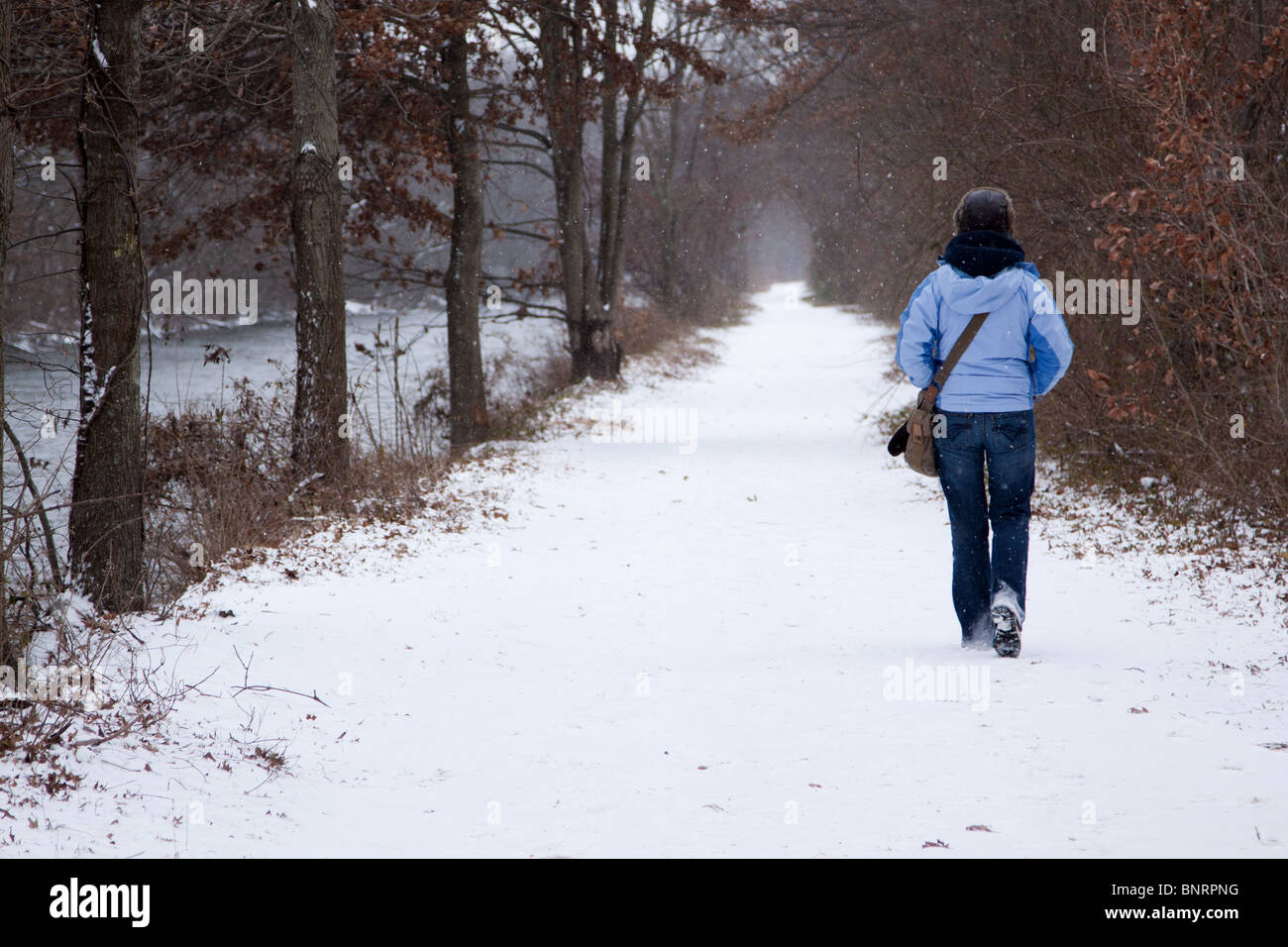 A woman walking beside a snowy riverside path in freezing cold winter ...