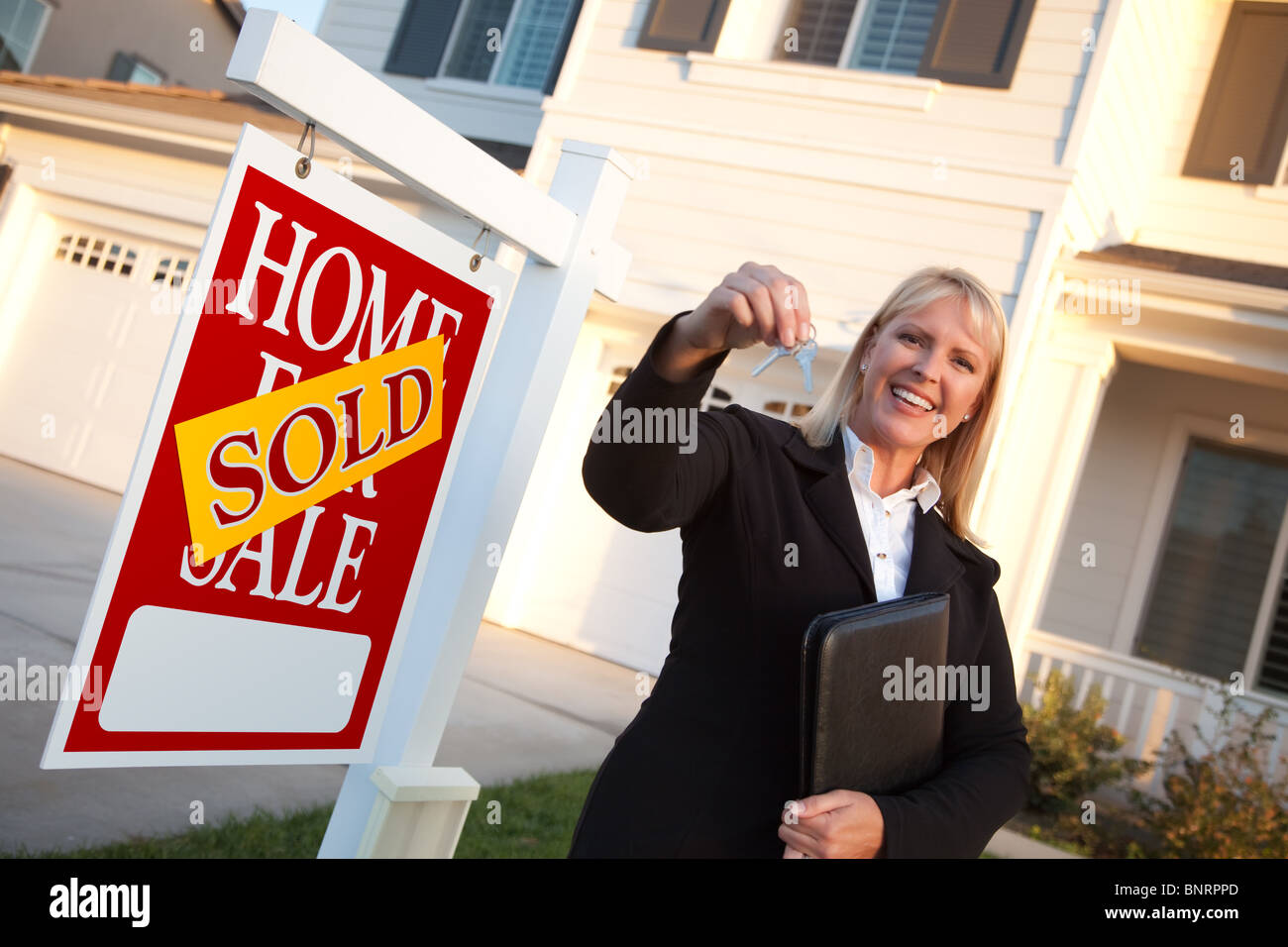 Female Real Estate Agent Handing Over the House Keys in Front of a Beautiful New Home and Real Estate Sign. Stock Photo