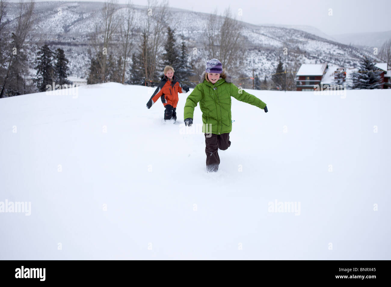 Siblings chasing each other in the snow. Stock Photo