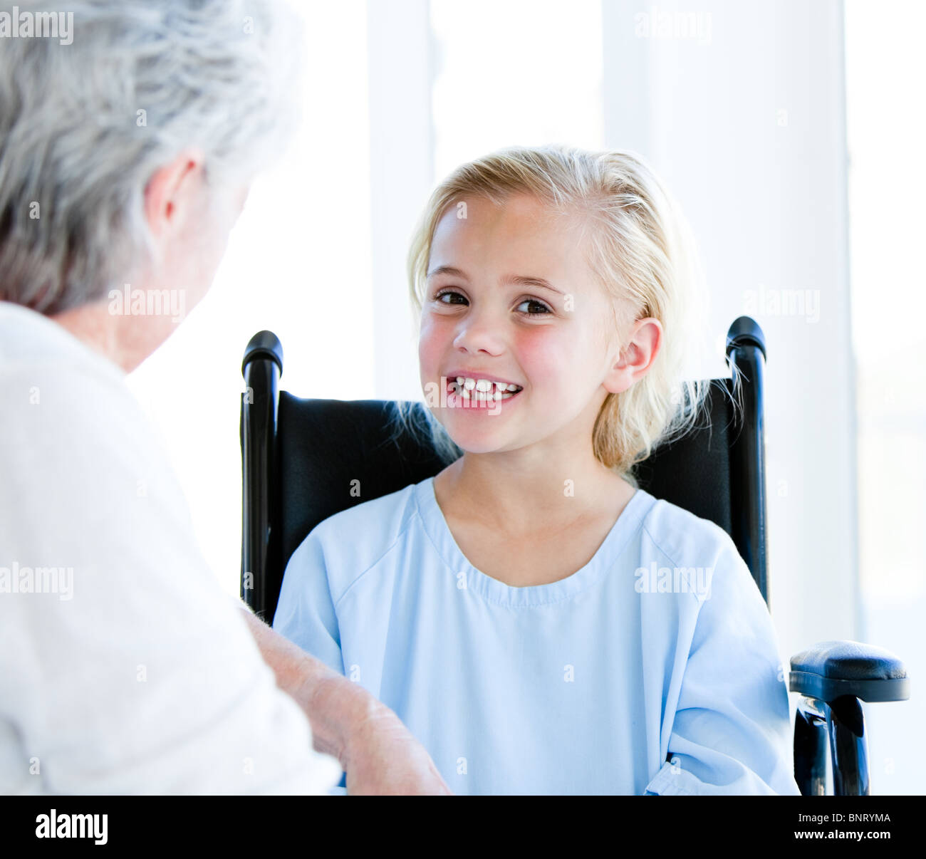 Blond little girl sitting on a wheelchair talking with her grandmother Stock Photo