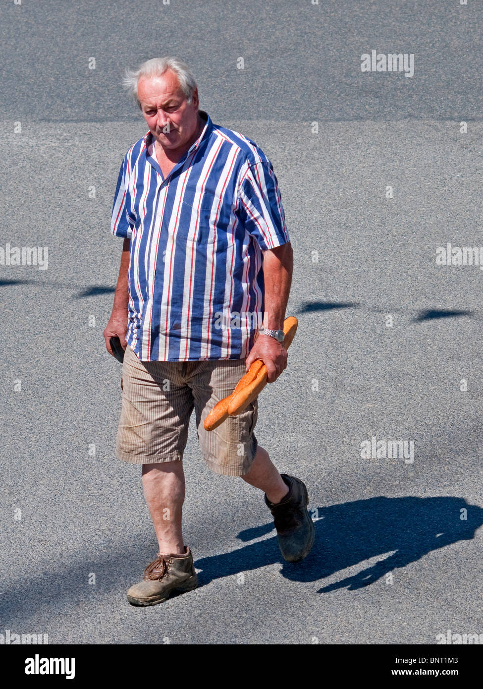 Man with baguettes walking across road - France. Stock Photo