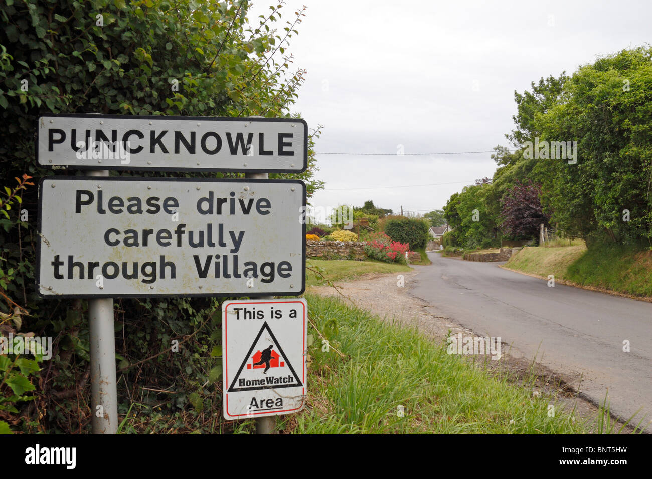 Road sign & 'Please drive carefully' sign at the entrance to the small Dorset village of Puncknowle, Dorset, UK. Stock Photo