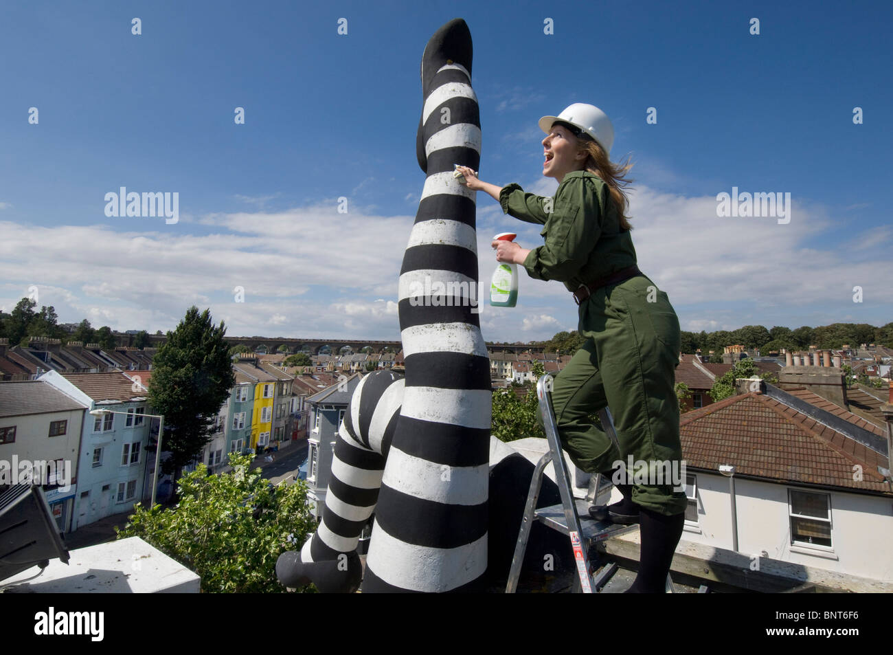 A blonde girl in overalls on a ladder on a rooftop cleaning a pair of giant legs. Duke of York Cinema, Brighton. Stock Photo