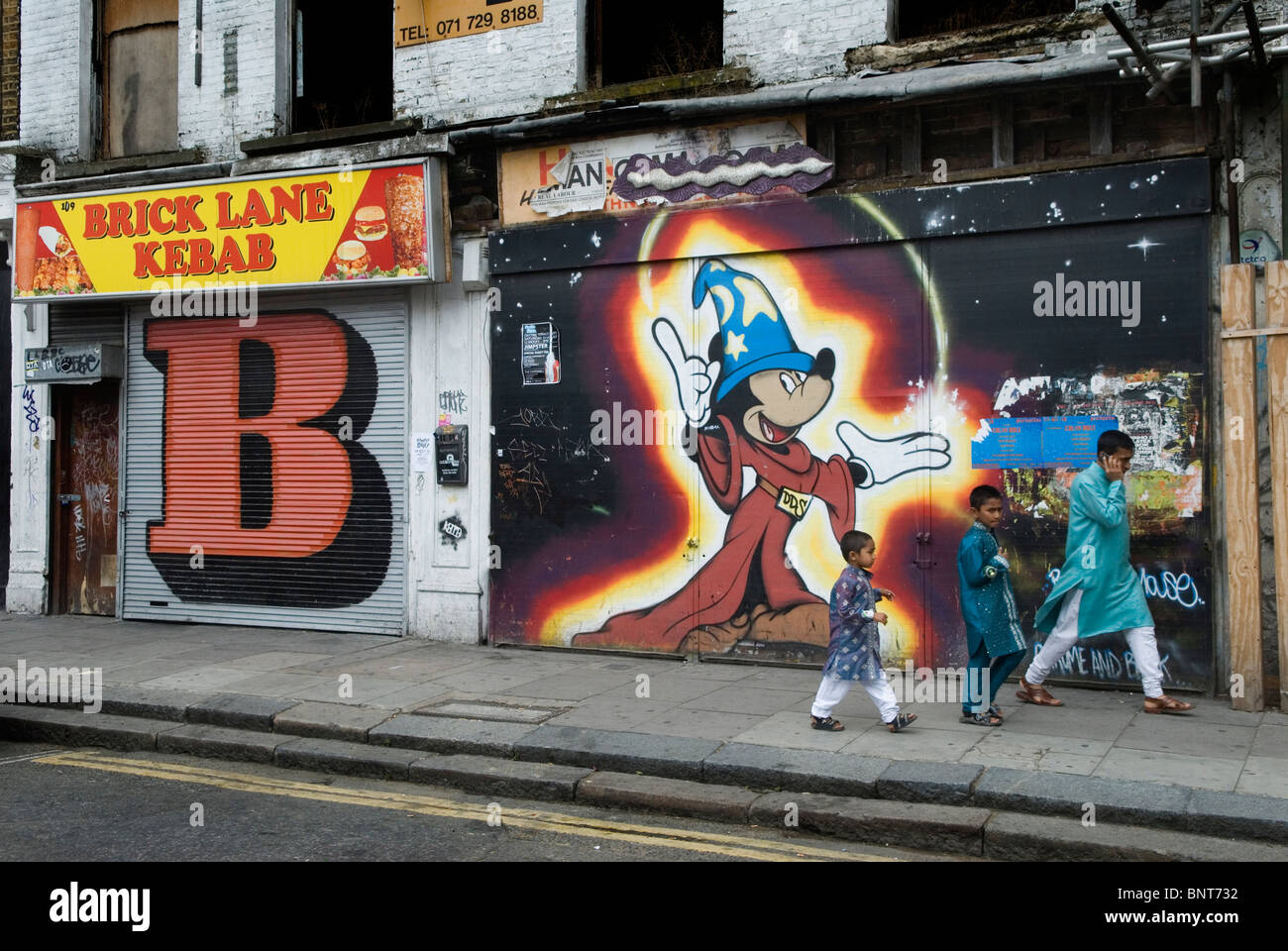 Brick Lane, east London. Muslim father sons return from Mosque walking past stencil street art by Ben Eine and DDS. 2010 2010s HOMER SYKES Stock Photo