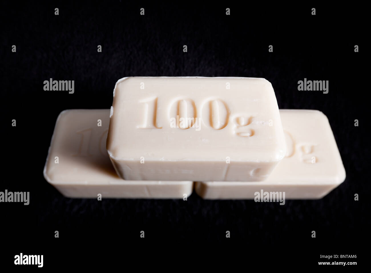 Three bars of plain soap stamped with 100g on a black towel Stock Photo