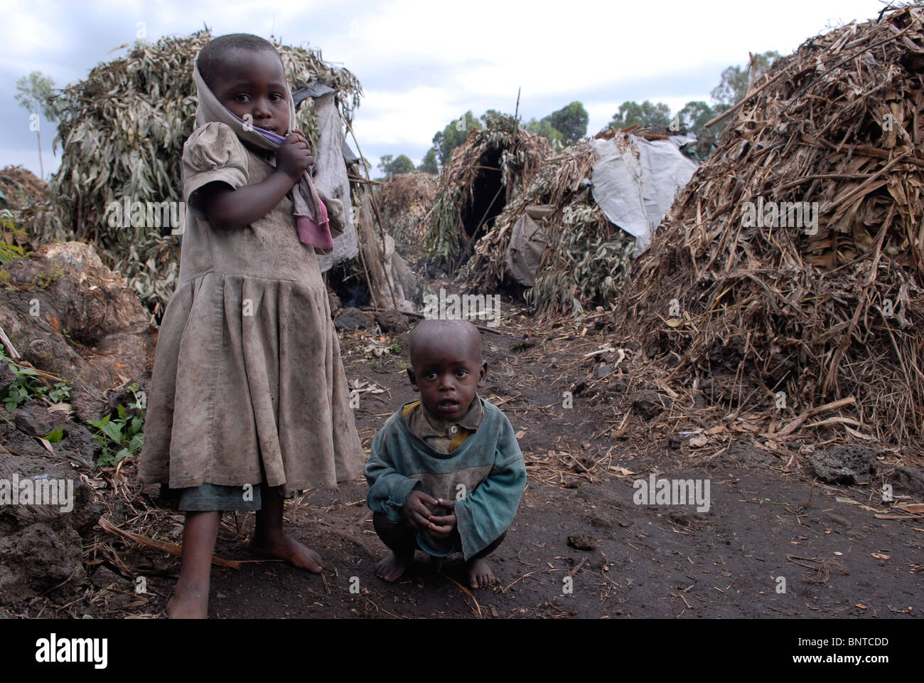 Young Displaced Congolese children stand amid makeshift straw huts in a makeshift IDP camp in North Kivu province DR Congo Africa Stock Photo