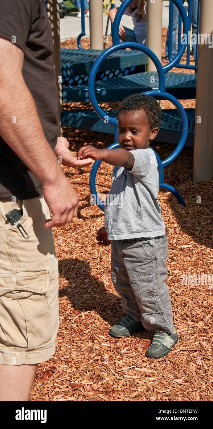 This adorable little African American toddler boy is handing a Caucasian man something from his tiny hand at a park while play. Stock Photo