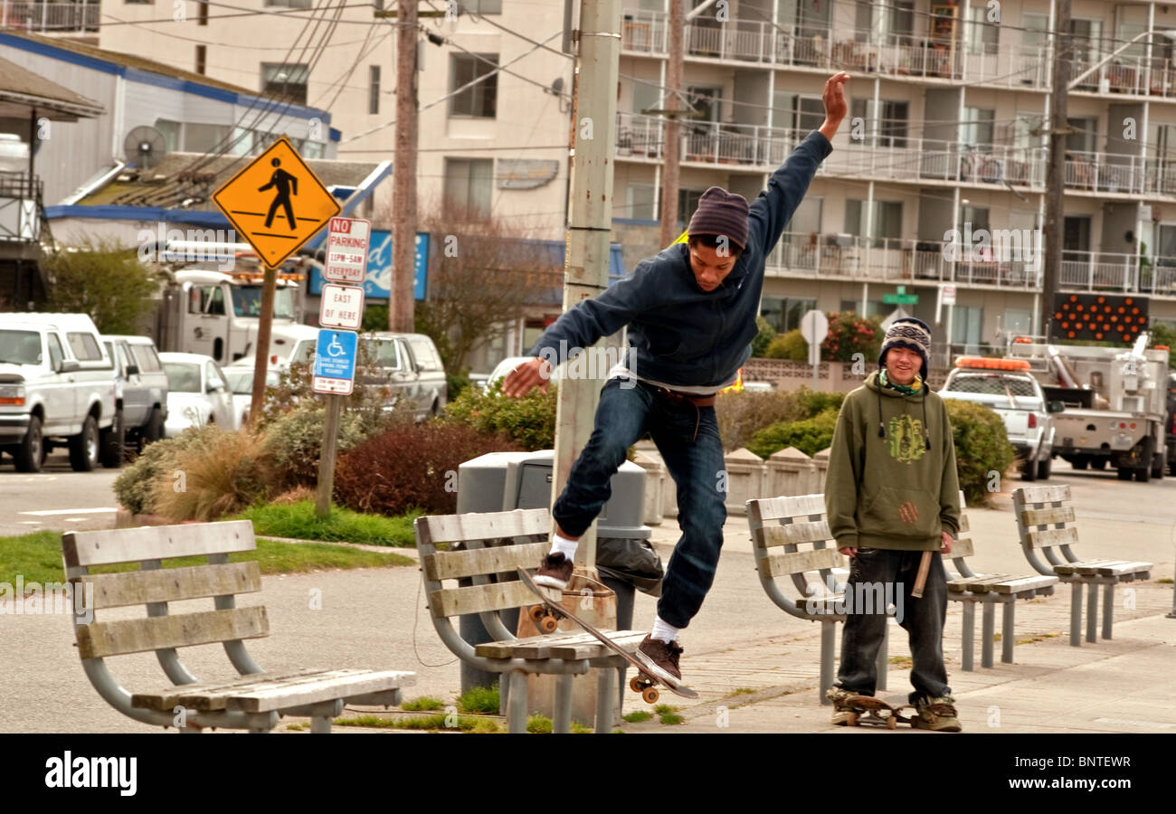 This African American teen is skateboarding off a city bench while his Asian friend is nearby watching in this urban city life. Stock Photo